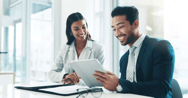 two smartly dressed people sit at desk with tablet